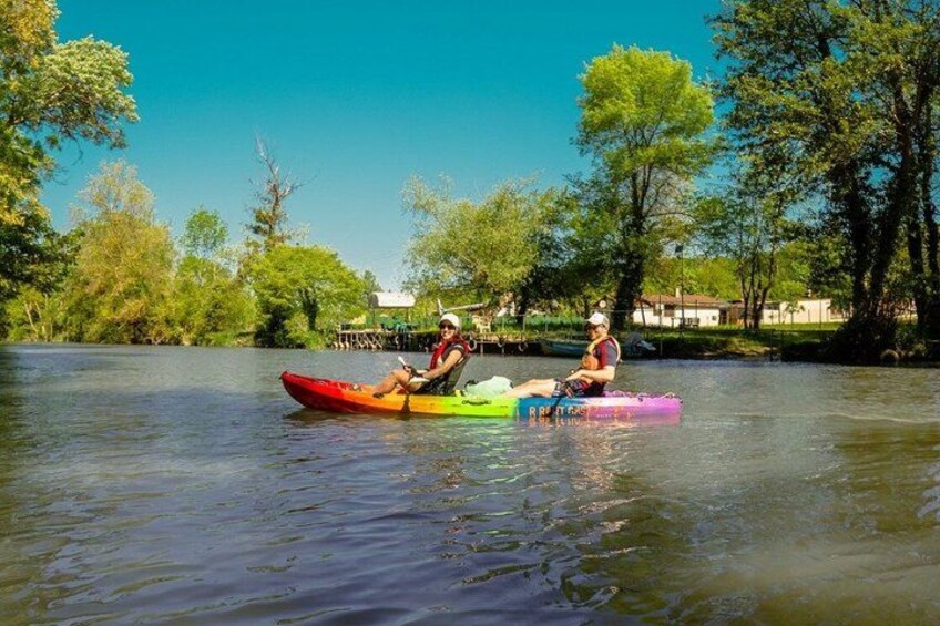 Two people kayaking on a calm river surrounded by trees and a clear sky. 2
