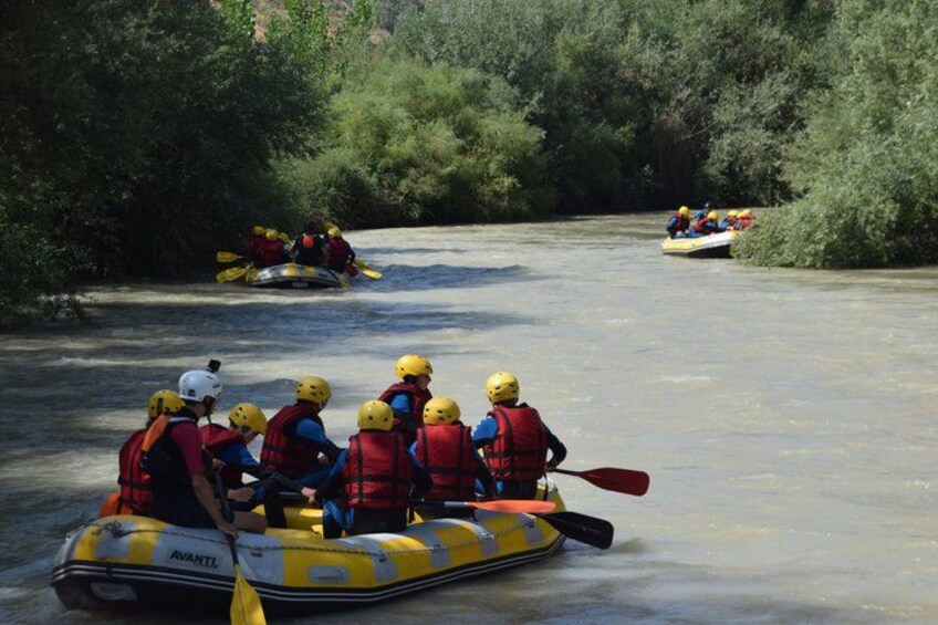 A group of people in a yellow inflatable raft navigating a river surrounded by dense greenery. 2