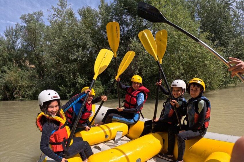 A group of people in a yellow inflatable raft on a river, paddling with yellow paddles. 1