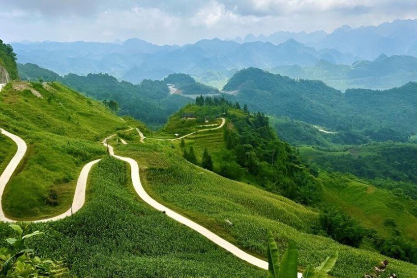 A winding road through lush green hills with distant mountains. 4