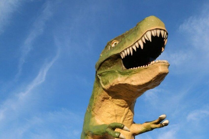 A large dinosaur statue with an open mouth and sharp teeth, set against a clear blue sky. 2