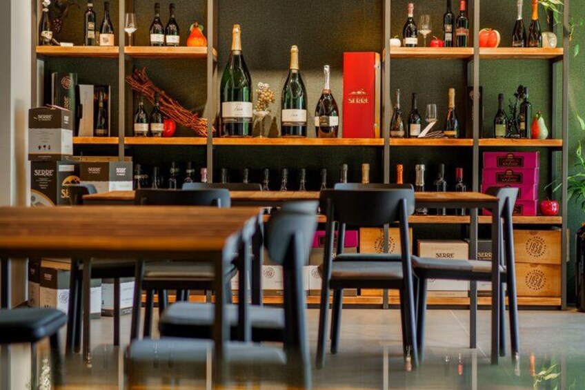 A bar with wooden shelves stocked with bottles and boxes, black chairs, and a polished floor. 5