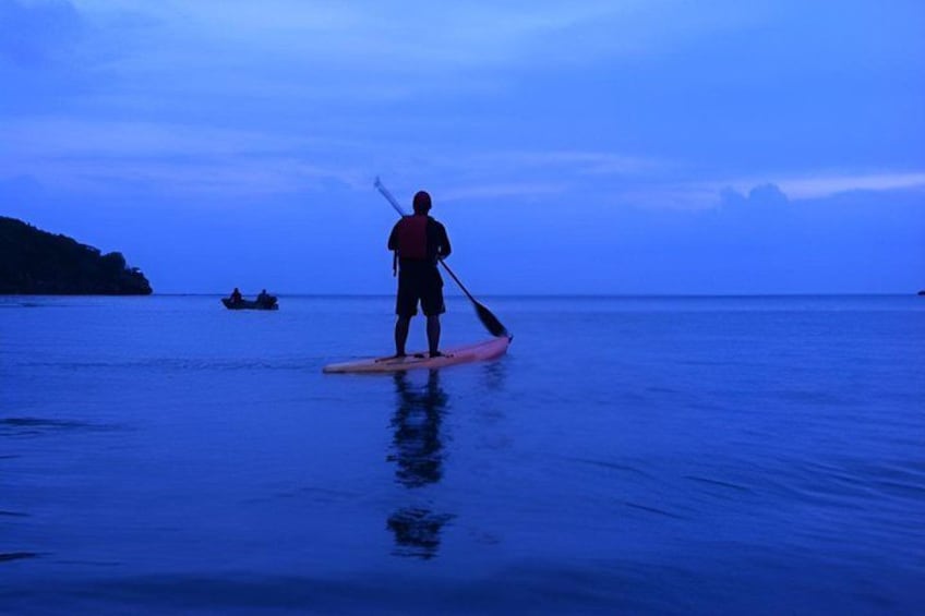 A person paddleboarding on calm water with a boat in the background. 3