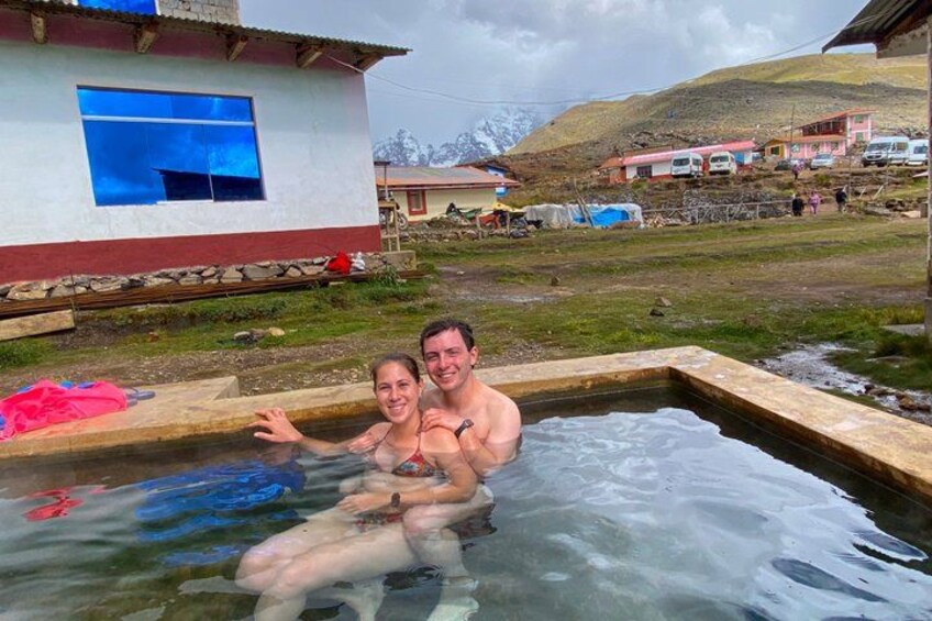 A couple in a hot spring with a building and mountains in the background. 5