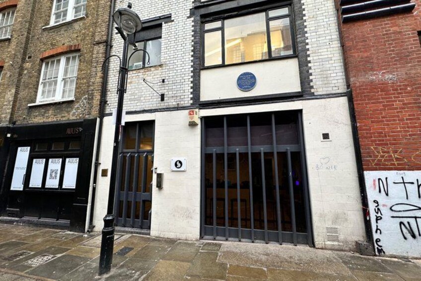 A building with a large window and a black door, a street lamp, and a brick wall with graffiti. 2