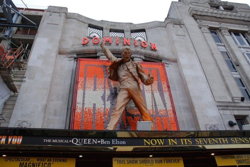 A theater with a large statue of a man, the sign 'DOMINION' above, and a marquee advertising 'THE MUSICAL QUEEN BEN ELTON'. 3