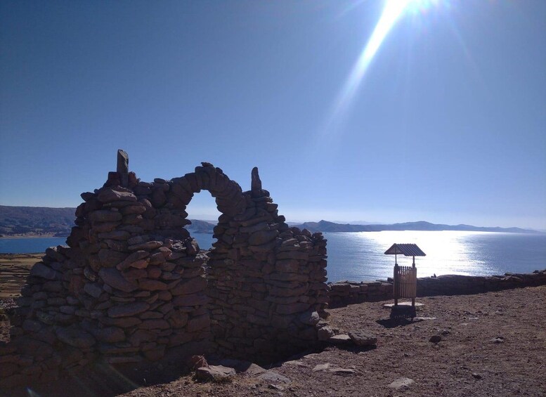 Eine steinerne Ruine mit einer kreisförmigen Öffnung, einer solarbetriebenen Lampe und Blick auf ruhiges Gewässer mit fernen Bergen unter blauem Himmel. 5