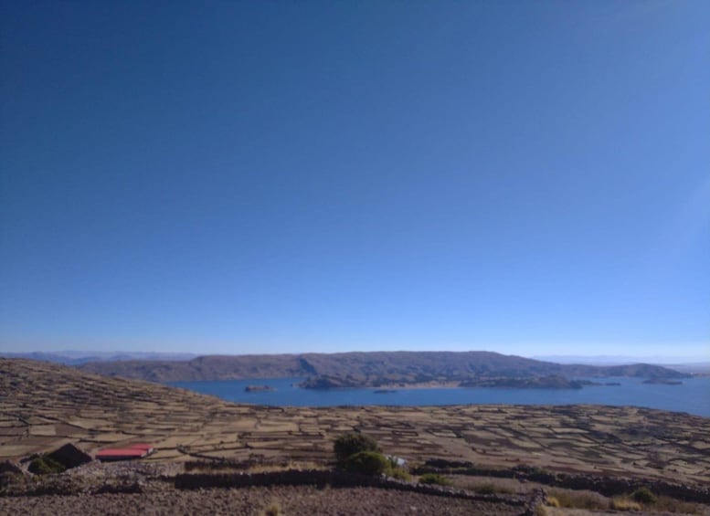 Eine Landschaft mit terrassenförmig angelegten Feldern, einem kleinen Gebäude mit rotem Dach und einer Wasserfläche in der Ferne. 2