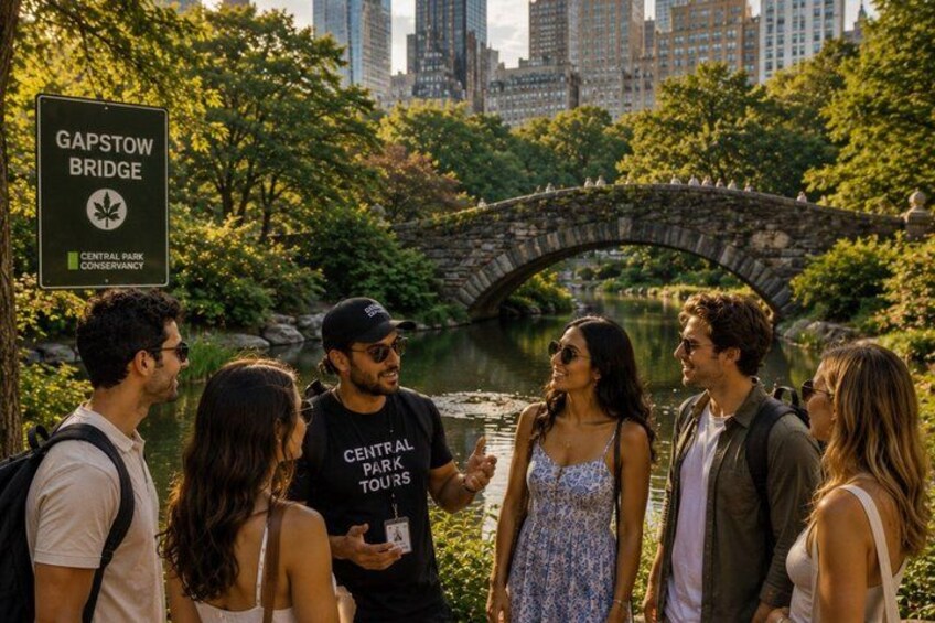 A group of people standing near a stone bridge with a sign that reads 'Gapstow Bridge' and 'Central Park Conservancy.' 2