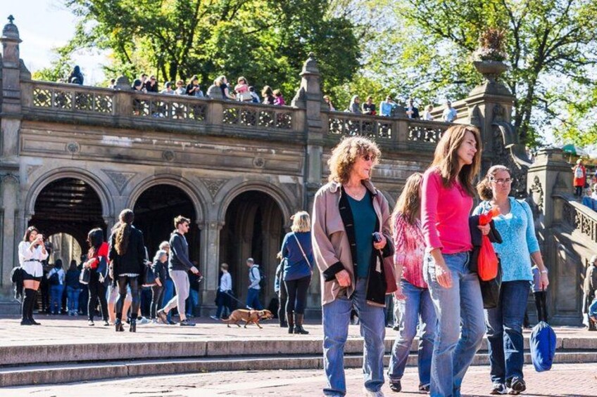 A group of people walking on a stone bridge with arches, surrounded by trees and a crowd of tourists. 4