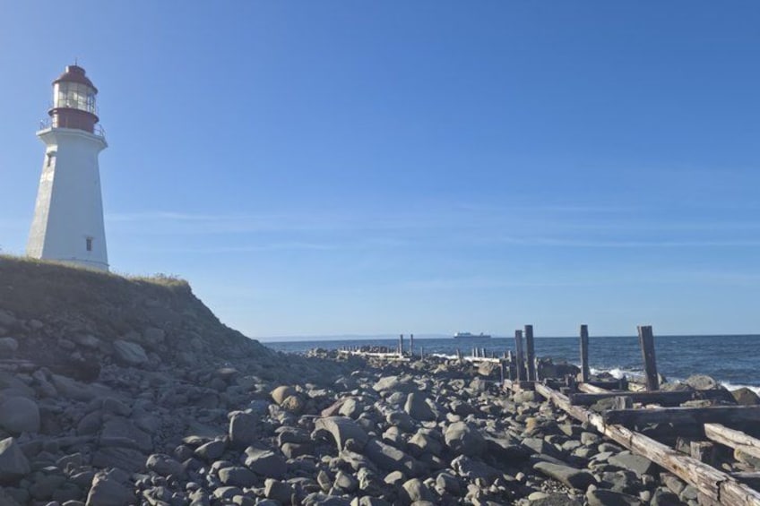 A lighthouse, rocky shoreline, and wooden posts. 1
