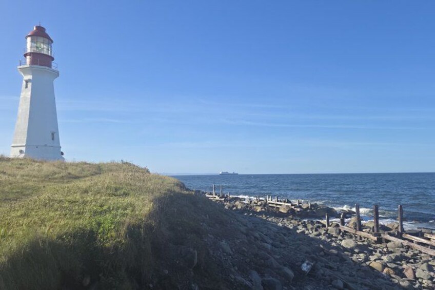 A lighthouse, rocky shoreline, and calm sea under a clear sky. 3