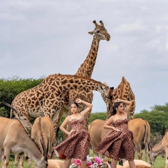 Une girafe et deux femmes dans un champ, entourées d’autres animaux. 2