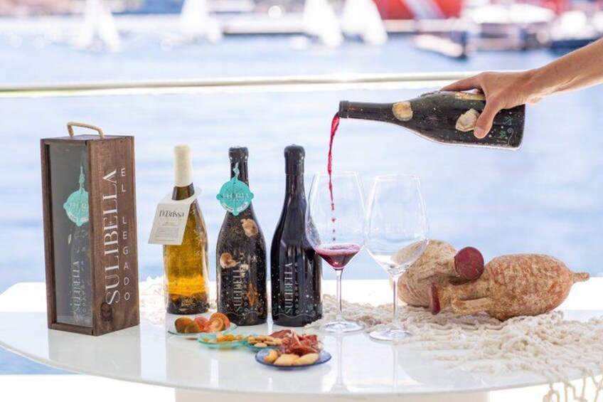 A table with wine bottles, glasses, and food items, with a person pouring wine. 1