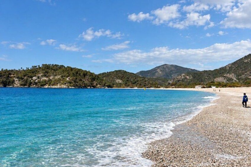 A clear blue sea, a pebbly beach, and a hilly landscape in the background. 5