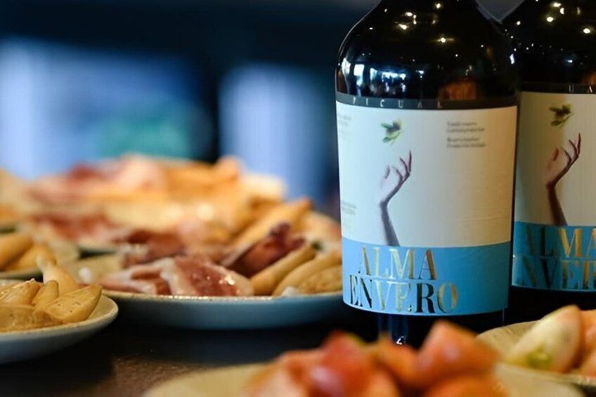 A bottle of Alma Vino with a label featuring a hand and a bird, placed on a table with plates of food. 2