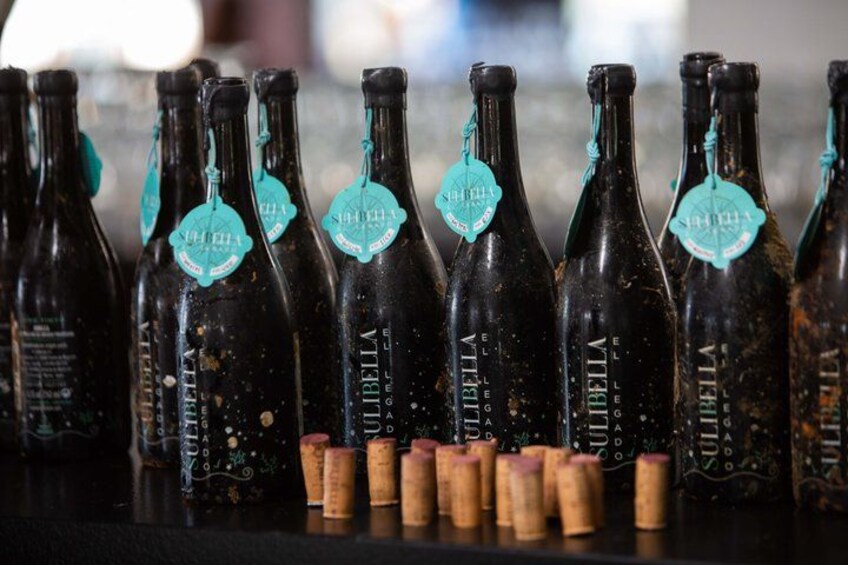 A row of dark bottles with tags, some corks, and a blurred background. 5