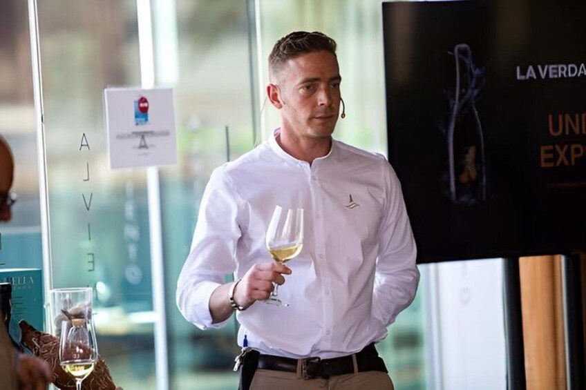 A person holding a wine glass in a modern indoor setting with glass walls and a poster in the background. 3
