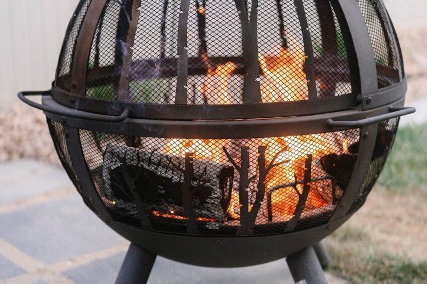 A metal fire pit with a mesh cover, burning wood, and a metal stand. 4