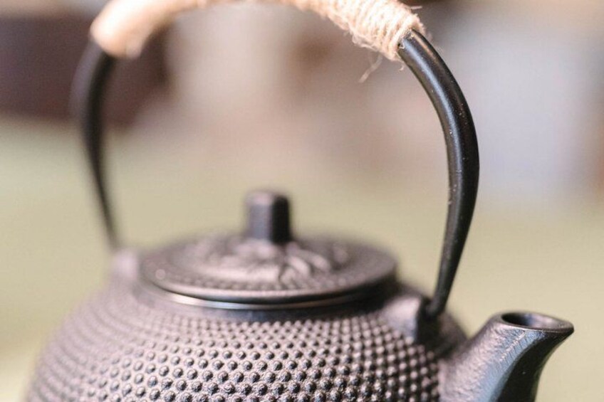 A close-up of a textured metal teapot with a handle wrapped in twine. 5