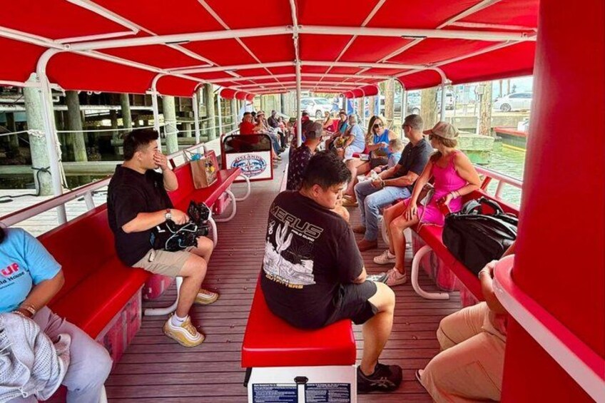 A red boat with passengers seated on benches, a wooden deck, and a canopy overhead. 3