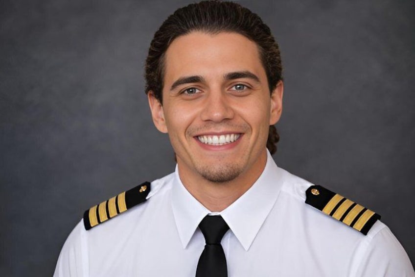 A person in a white shirt with black and gold epaulettes, a black tie, and a black lapel pin. 5