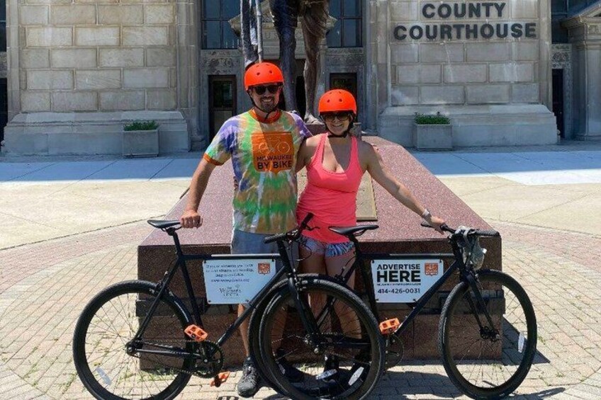 Two people standing next to a bicycle with a sign that reads 'ADVERTISE HERE' in front of a building labeled 'COUNTY COURTHOUSE.' 4