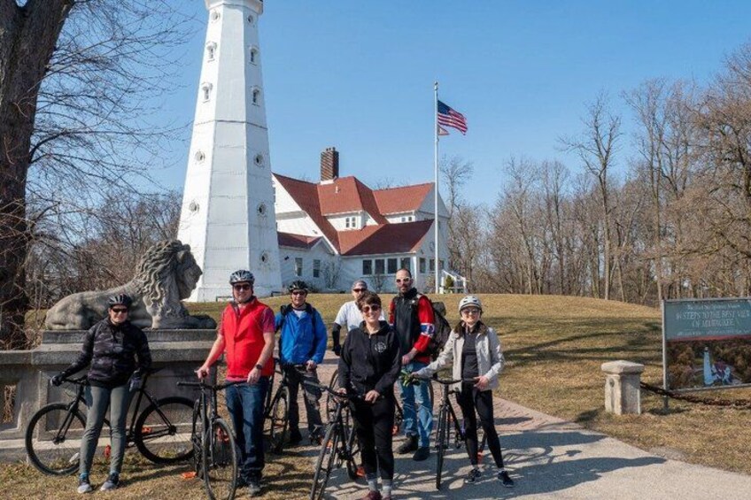 A group of people with bicycles in front of a lighthouse and a building with a red roof. 5