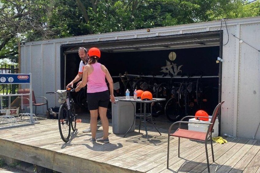 A covered area with a bicycle, a person wearing a helmet, and a table with a helmet on it. 3