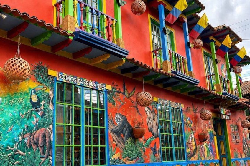 A colorful building with murals, a sign reading 'SOMOSEFABRICANTES,' and a balcony with hanging decorations. 5