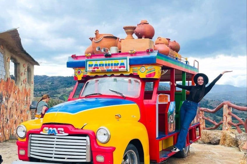 A colorful, decorated vehicle with the word 'FARQUIRA' on it, parked on a dirt path with a mountainous landscape in the background. 4