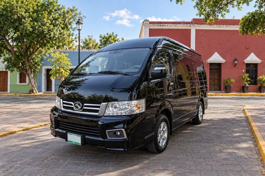 A black van parked on a paved street with a red building in the background. 2