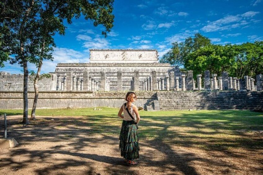 A person standing in front of a large ancient Mayan pyramid with a clear sky. 5