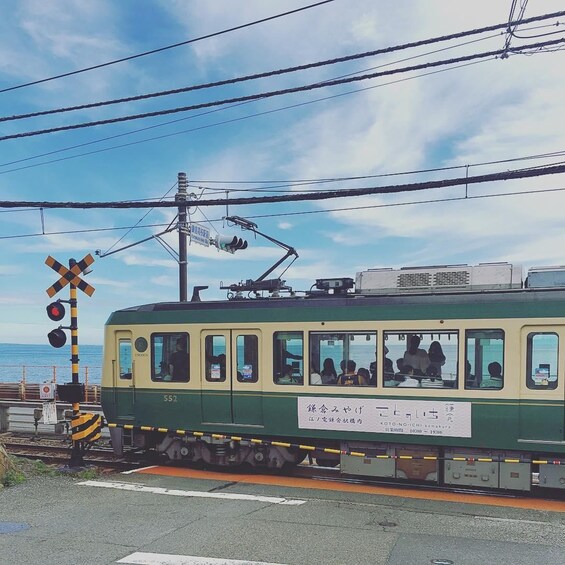 A green and yellow tram at a railway crossing with a signboard and a clear sky. 4