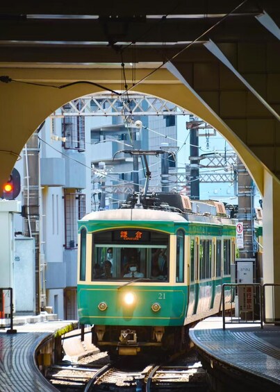A green tram at a station with a large overhead structure. 5