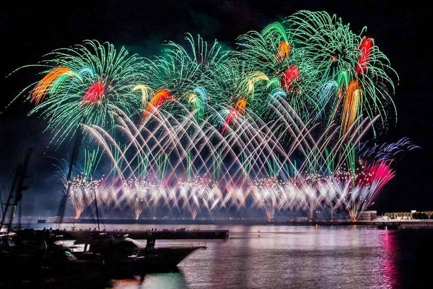 A nighttime fireworks display over a body of water with reflections. 1