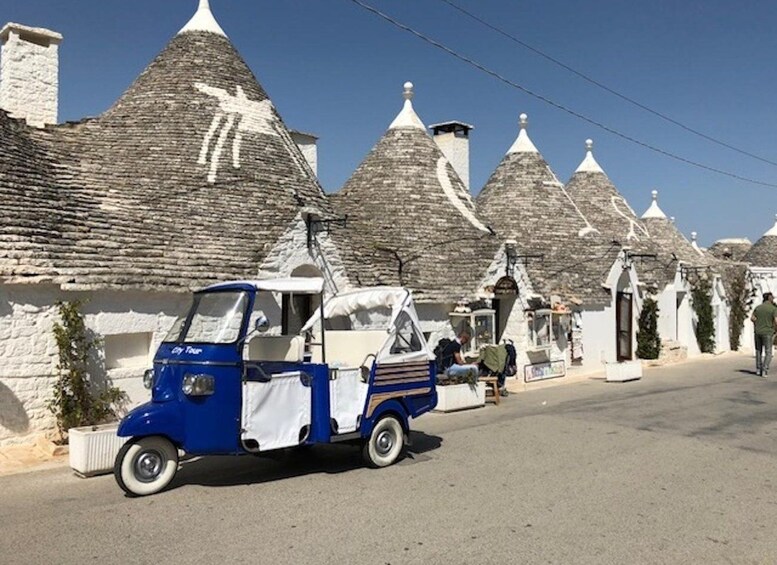 Sininen ja valkoinen tuk-tuk on pysäköity kadulle, jonka varrella on perinteisiä kivitaloja, joissa on kartiomaiset katot. 2