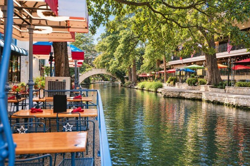 A riverside restaurant with outdoor seating, a bridge, and trees. 1