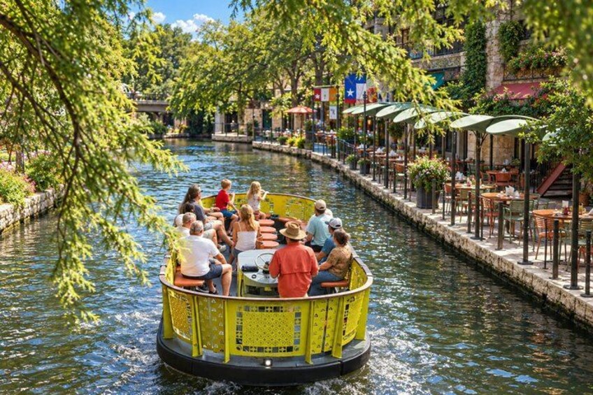 A yellow boat with people on a canal surrounded by outdoor seating areas and flags. 4