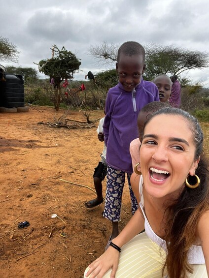 A woman taking a selfie with two children in a dry, open landscape with sparse vegetation and a cloudy sky. 3