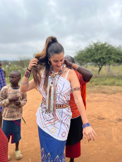 A person in traditional attire with intricate beadwork, standing outdoors with a child in the background. 4