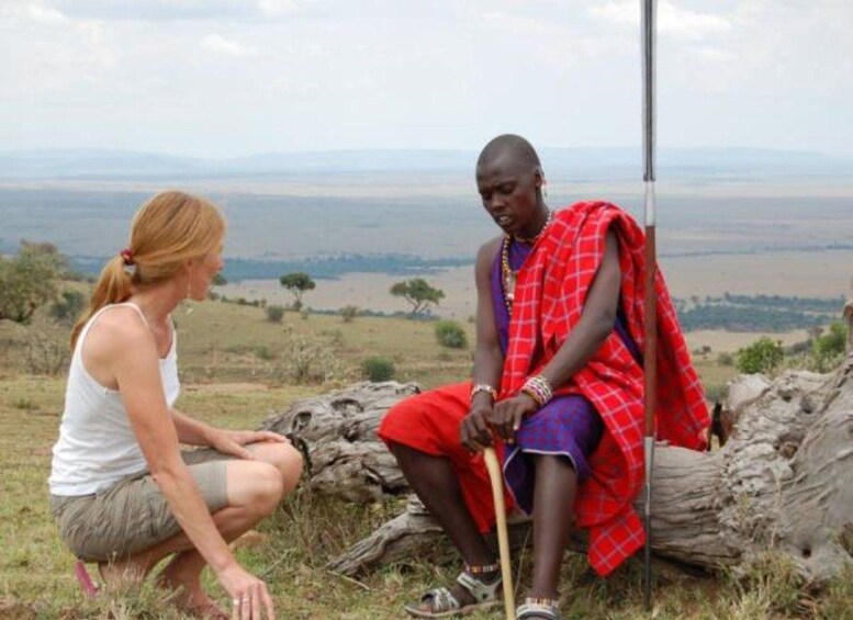 A person in traditional attire sitting on a log with a woman in casual clothing. 2