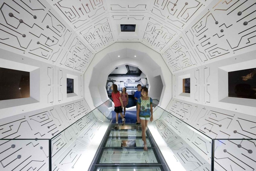 Un intérieur futuriste avec un escalier mécanique central, entouré d’un décor blanc évoquant un circuit imprimé. 4