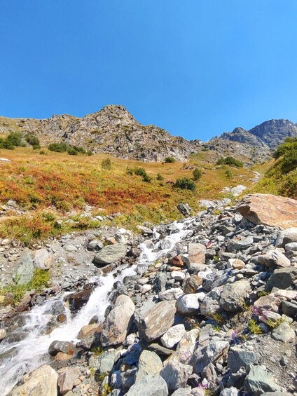 Un arroyo serpentea por un paisaje montañoso con vegetación escasa y cielos azules despejados. 4