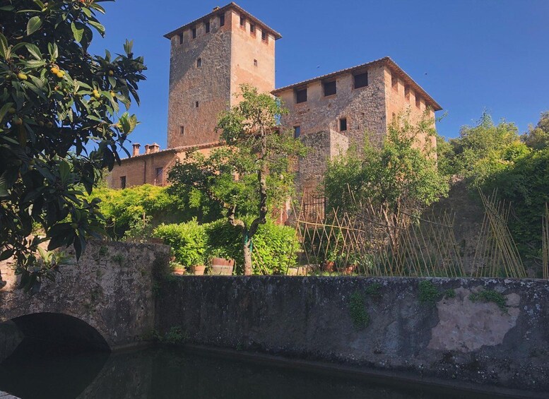 A historic stone tower and building complex surrounded by lush greenery and a stone bridge. 1