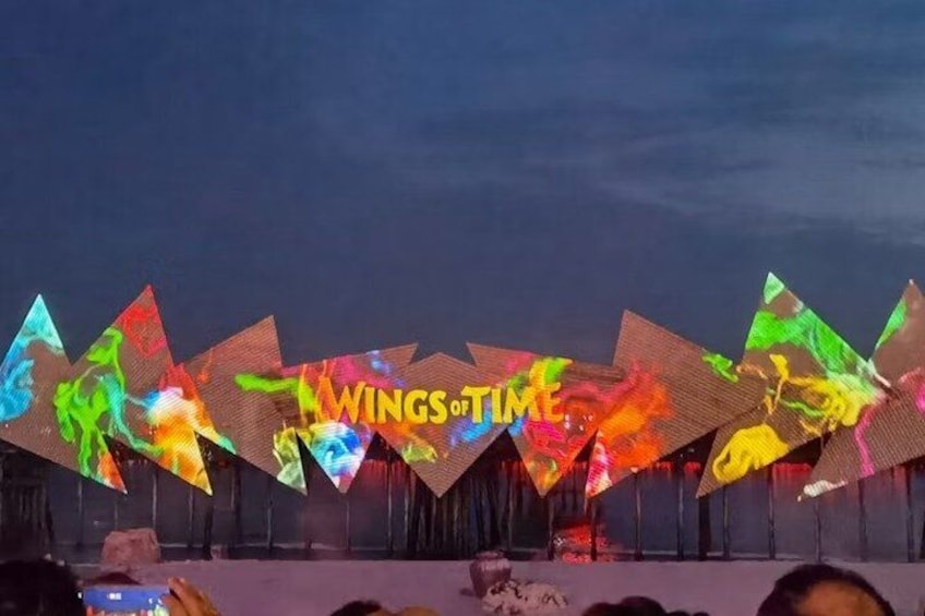 A nighttime outdoor event with illuminated triangular structures and the text 'WINGS of TIME' on a stage. 5