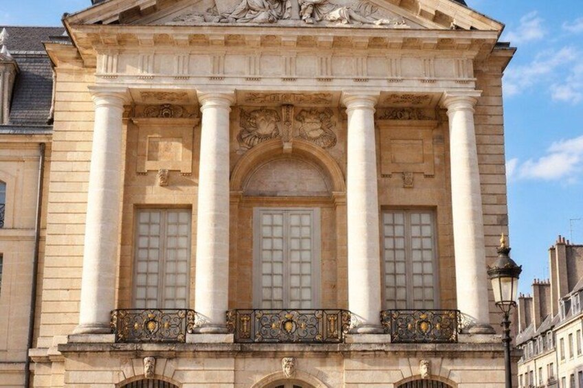 A classical building with columns, a pediment, and a balcony with ornate balustrades. 4
