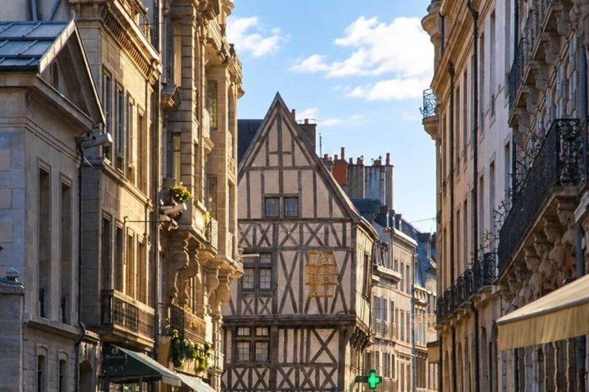 A narrow street with traditional half-timbered buildings, a clear sky, and a green traffic light. 2