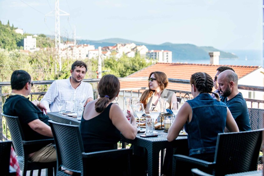 Un groupe de personnes est assis à une table en plein air, avec une vue panoramique sur les bâtiments et les collines en arrière-plan. 2
