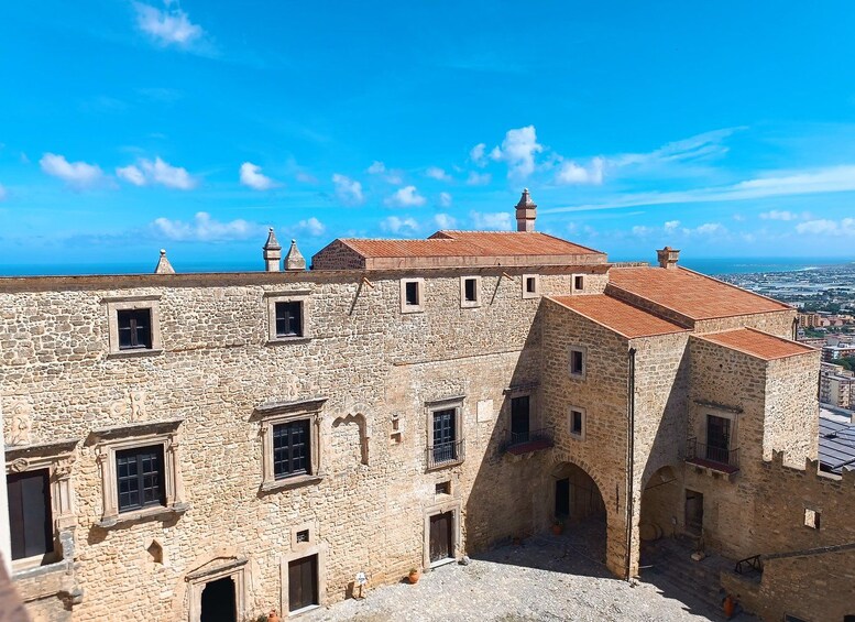 A stone building with arched doorways and windows, a red-tiled roof, and a view of the city below. 3